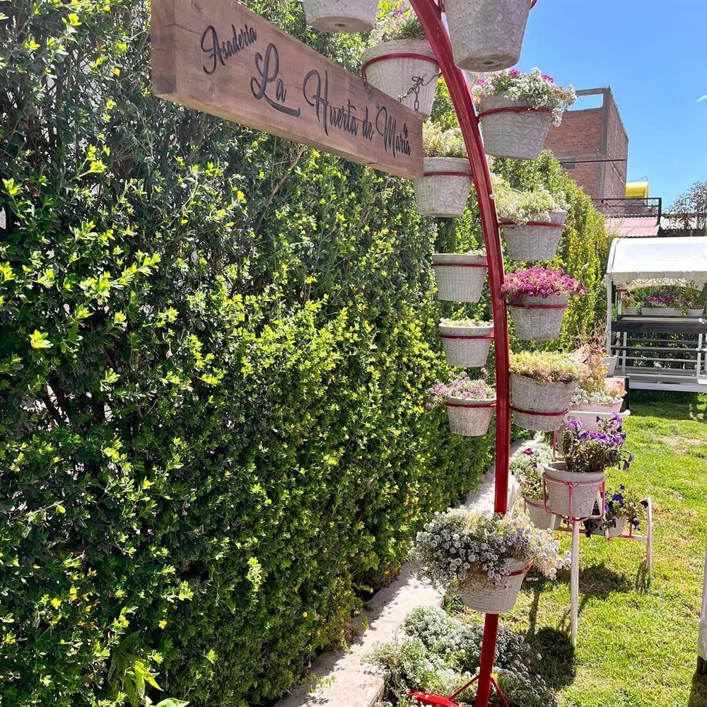 Entrada de La Huerta de María con su letrero de madera, jardín y macetas con flores